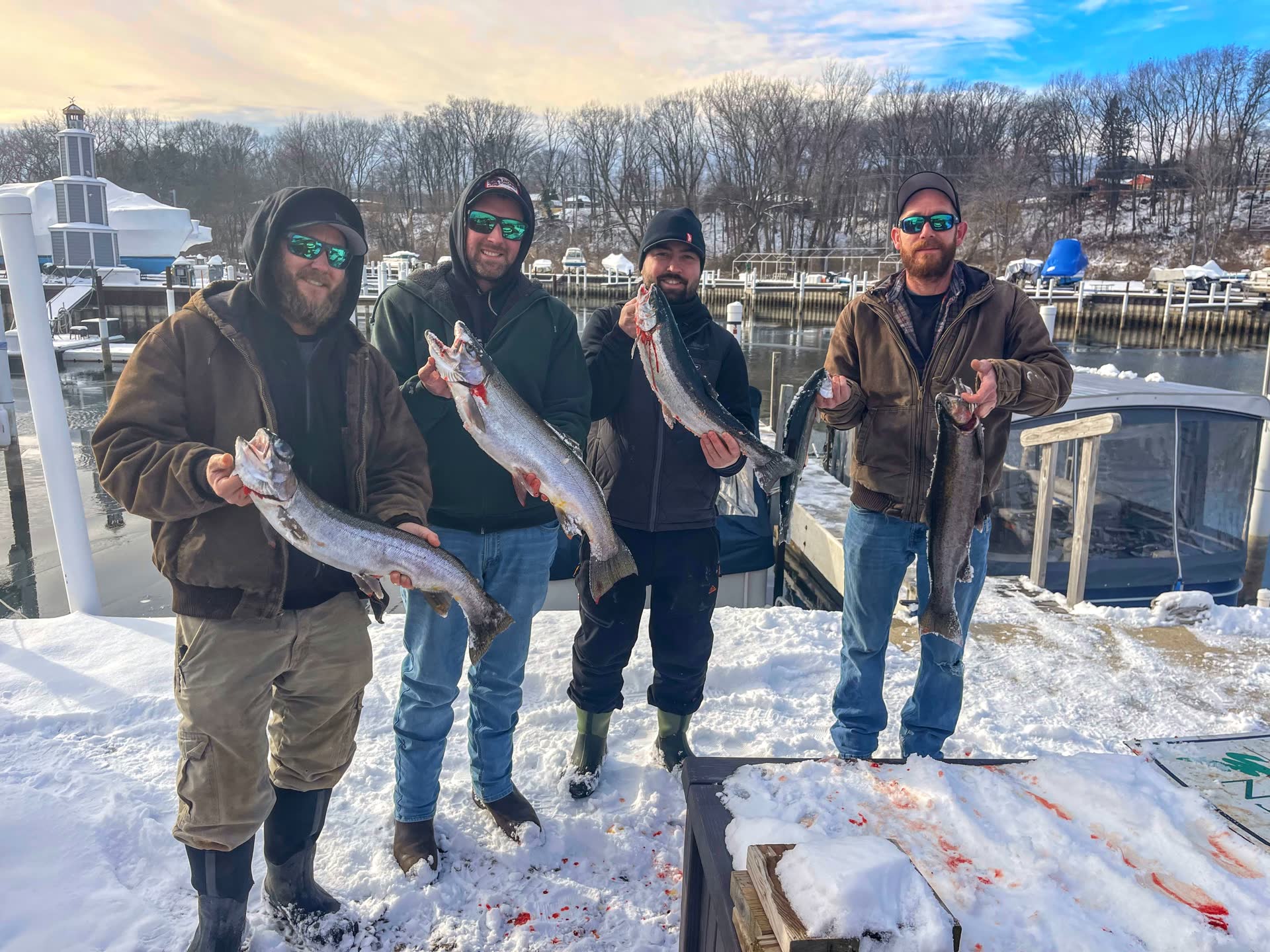 Four anglers on the St. Joseph dock in winter, holding steelhead they caught with the local charter.